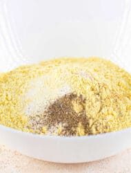 A white bowl brimming with a blend solid for fish fry, combining cornmeal, pepper, and flour.