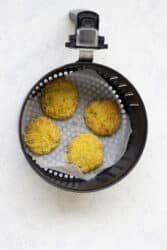 Four uncooked cod fish cakes rest in an air fryer basket lined with parchment paper.