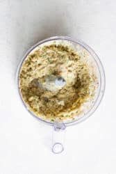 A food processor containing a coarse, creamy mixture of herbs and spices sits on a light countertop, ready to be transformed into good cod fish cakes.
