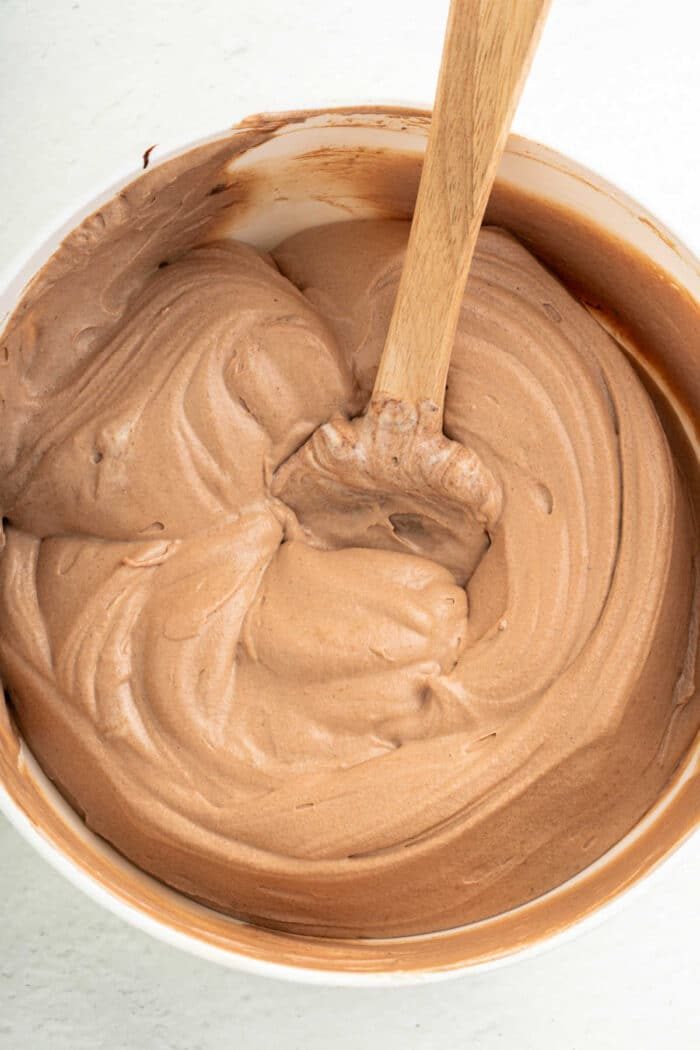 A wooden spoon in a bowl of creamy coffee frosting.