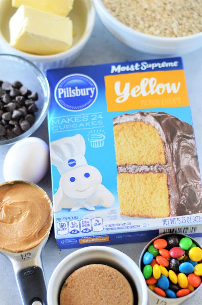 Box of Pillsbury yellow cake mix surrounded by butter, chocolate chips, egg, peanut butter, and candy—solid for making good Cookie Bars From Cake Mix.