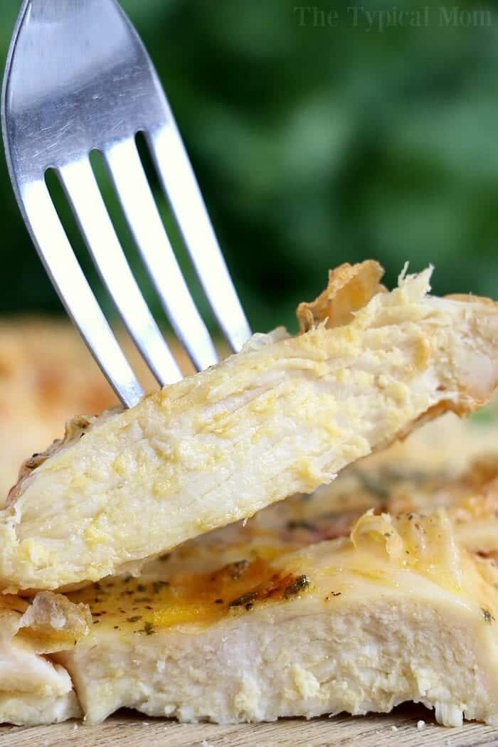 A fork holds a cooked chicken breast slice, showcasing its tender and juicy interior achieved by cooking a frozen chicken breast in an air fryer. The meat is seasoned with herbs and spices, while the background blurs into soothing shades of green.