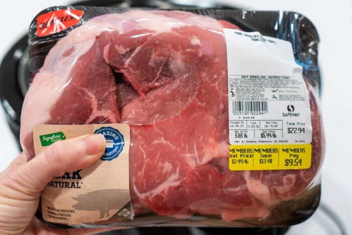 Hand holding packaged raw pork shoulder roast with price and weight labels visible—solid for cooking pulled pork.
