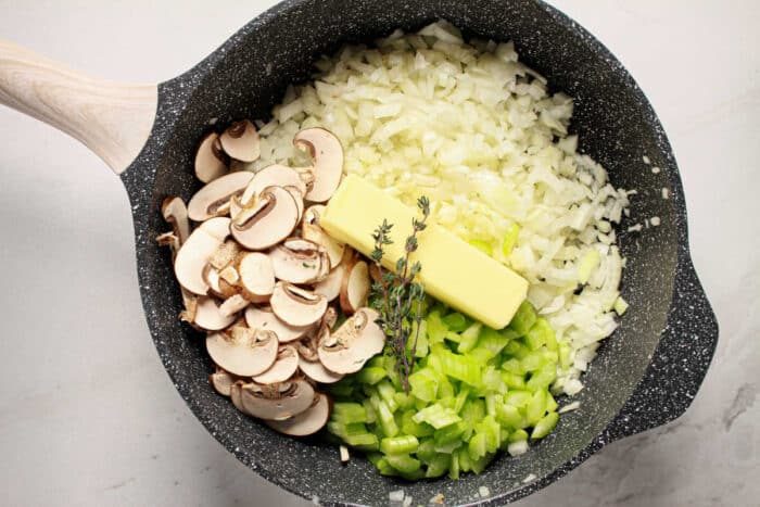Chopped onions, celery, mushrooms, butter, and thyme in a skillet, solid as a base for Jiffy Cornbread Stuffing.
