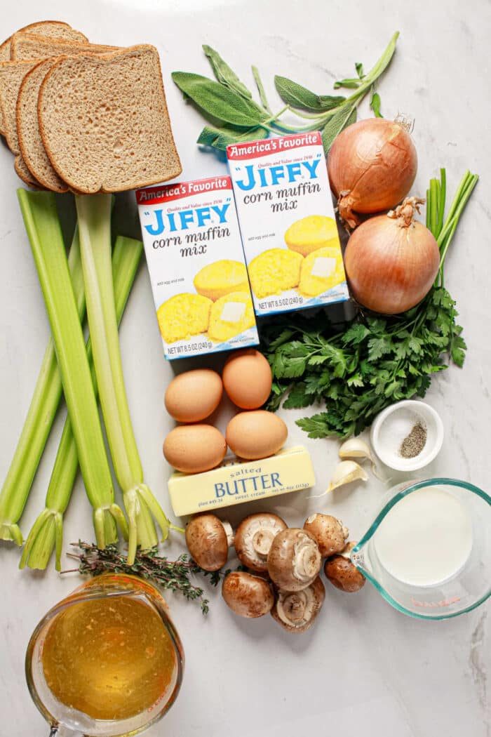 Ingredients for stuffing laid out: bread, Jiffy Cornbread mix, eggs, butter, celery, onions, mushrooms, herbs, broth, and milk—solid for a flavorful Cornbread Stuffing.