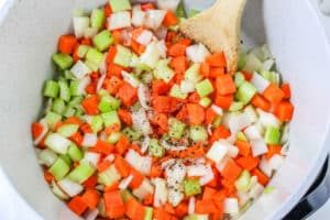 Chopped carrots, celery, and onions are stirred with a wooden spoon in a white pot—the flavorful base for hearty Corned Beef and Cabbage Soup.