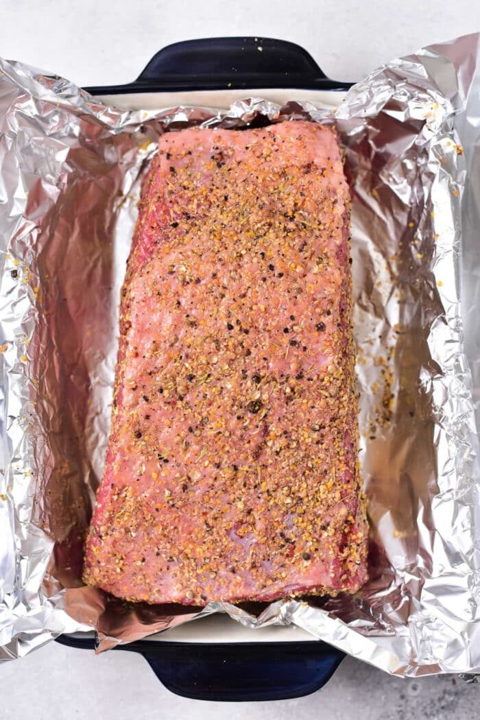 Seasoned with spices, the raw corned beef roast is prepared as a base for a delectable corned beef sandwich recipe, placed in a foil-lined baking dish for roasting perfection.