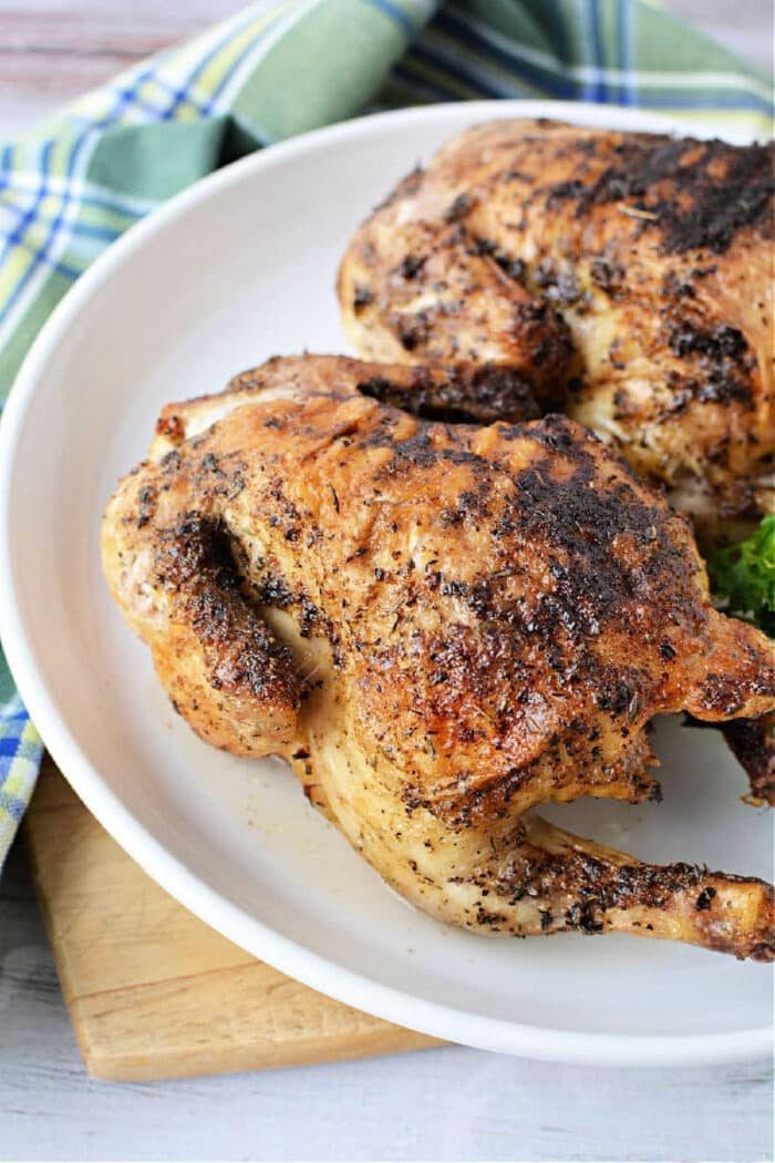 Two roasted, seasoned Cornish hens on a white plate with a plaid cloth in the background, solid for learning how long to cook Cornish hen in air fryer for tender, flavorful results.