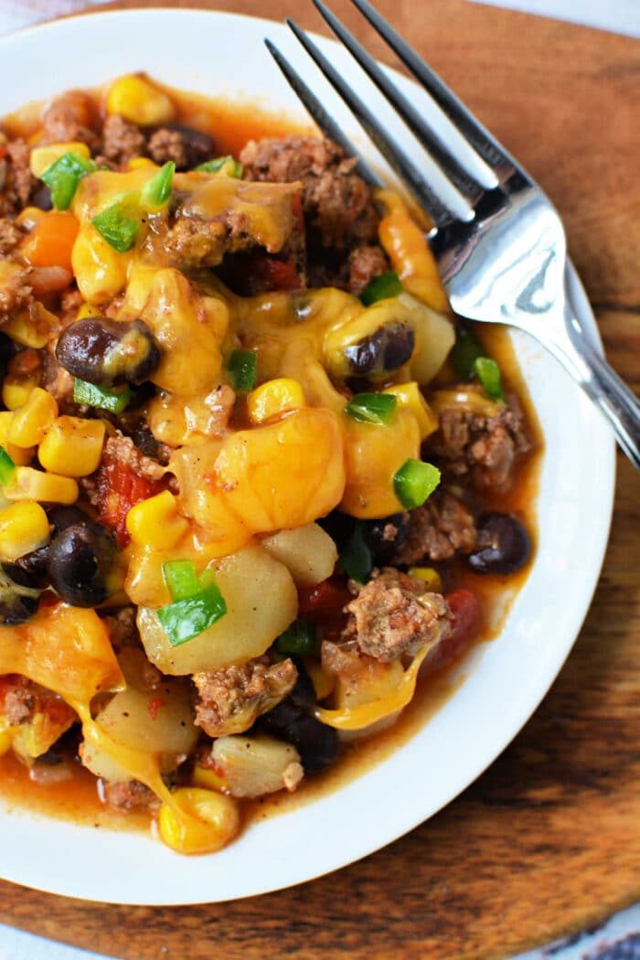 A plate of cheesy Cowboy Casserole with beef, black beans, corn, and potatoes sits next to a fork—solid for fans of hearty Crockpot recipes.