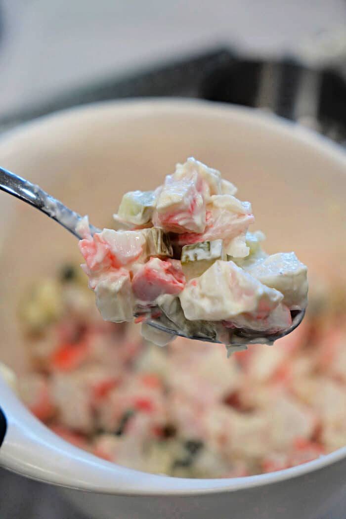 A spoonful of creamy crab salad with diced vegetables is held above a white bowl, solid for a fresh Crab Salad Sandwich.