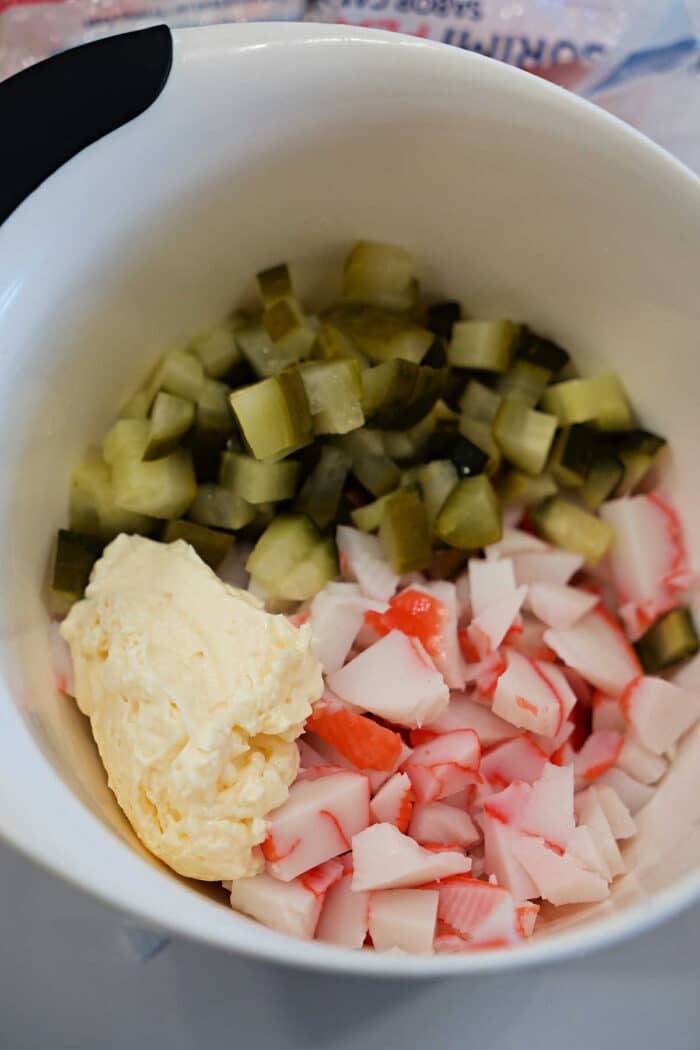 Chopped pickles, imitation crab meat, and mayonnaise in a white mixing bowl.