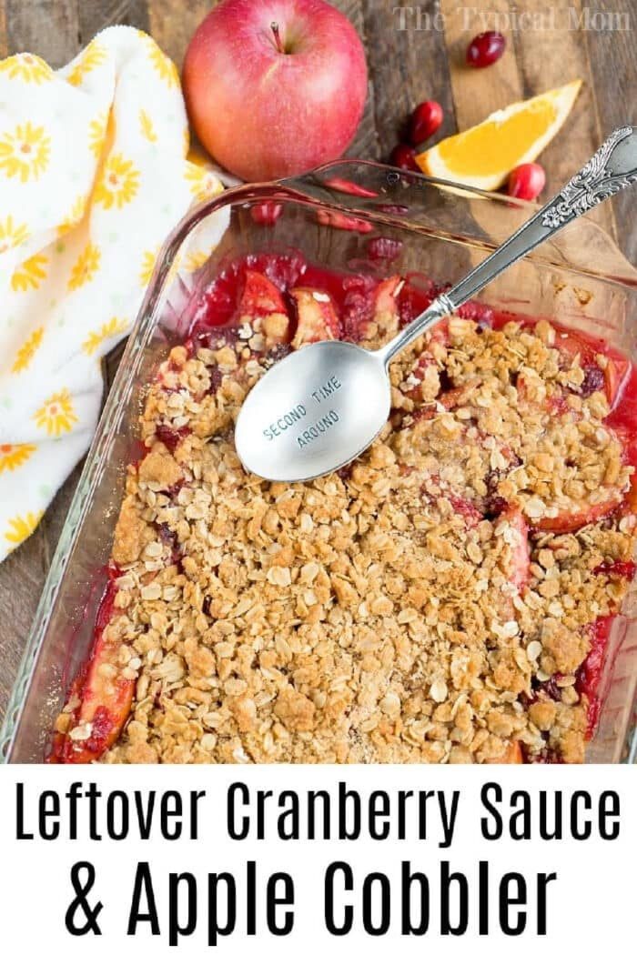 A dish of cranberry apple cobbler with a spoon, an apple, a lemon wedge, and cranberry sauce on the side.