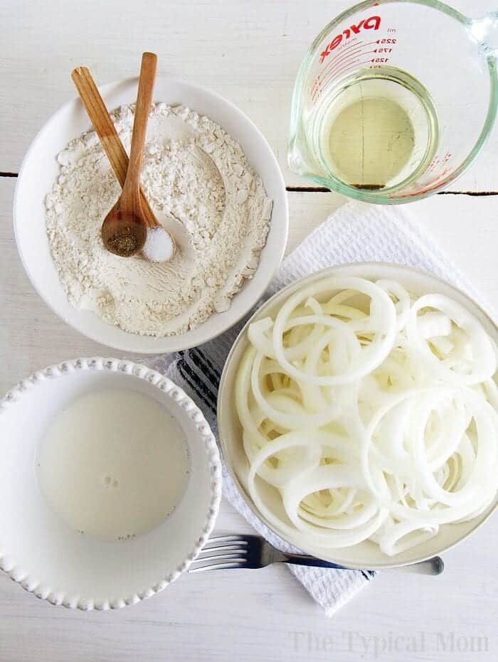 Bowl of flour, milk, crispy fried onions, and oil with utensils on a white surface.