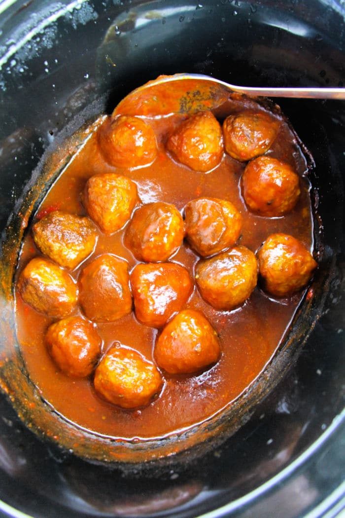Savor the delectable crockpot grape jelly meatballs, simmering in a rich, reddish-brown sauce, perfectly presented with a spoon.