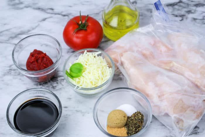 Ingredients for a recipe: Crockpot Chicken Frozen Breasts, tomato, olive oil, cheese, seasonings, tomato paste, and balsamic vinegar.
