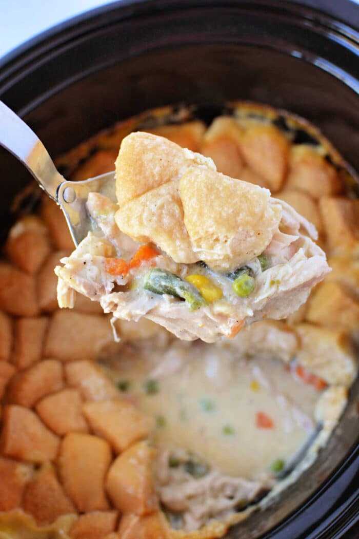 A spoon lifts creamy chicken and vegetables with biscuit topping from a slow cooker, capturing all the comforting flavors of Chicken Pot Pie in one good scoop.