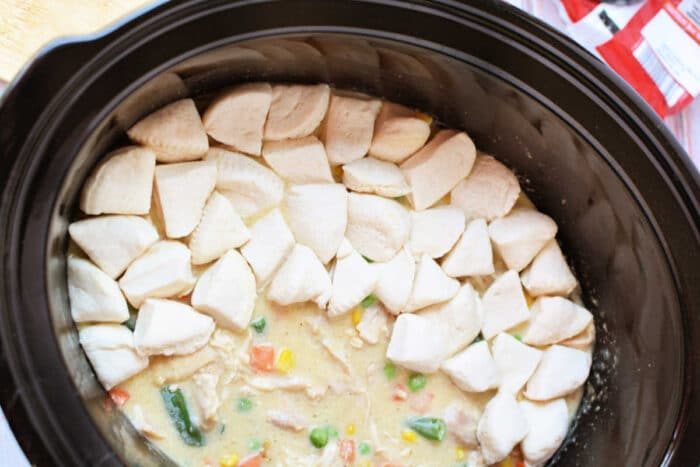Crockpot Chicken and vegetable stew in a slow cooker, topped with raw biscuit dough pieces arranged in a ring for a good twist on classic Chicken Pot Pie.