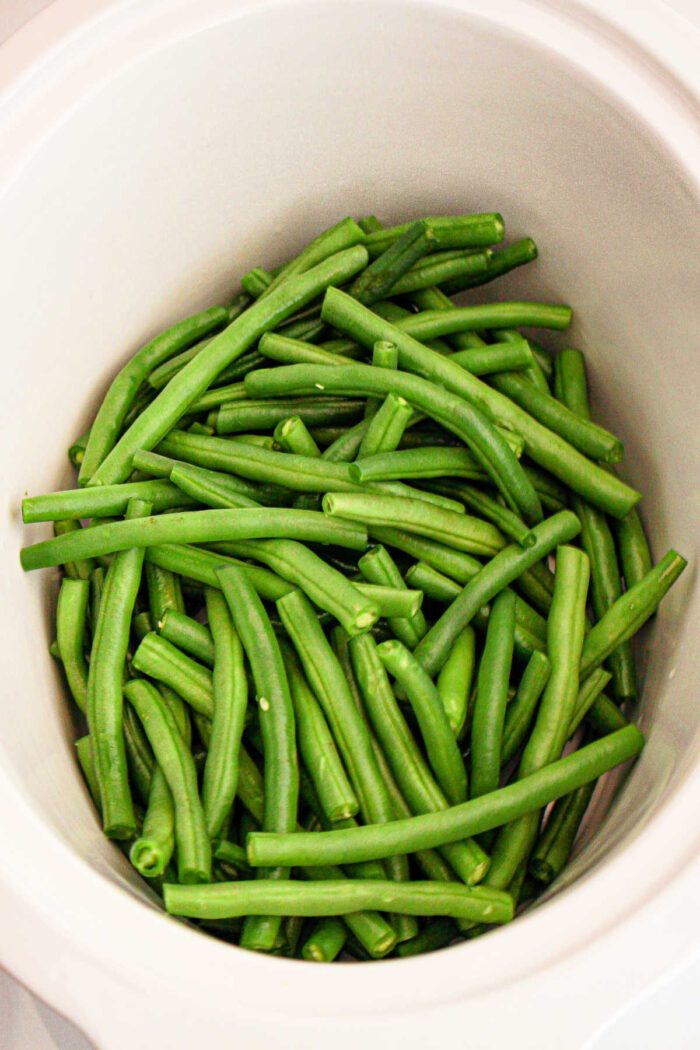 A slow cooker is filled with a pile of raw green beans, freshly cut and vibrant in color, waiting to be prepared or added to your crockpot for a good meal.