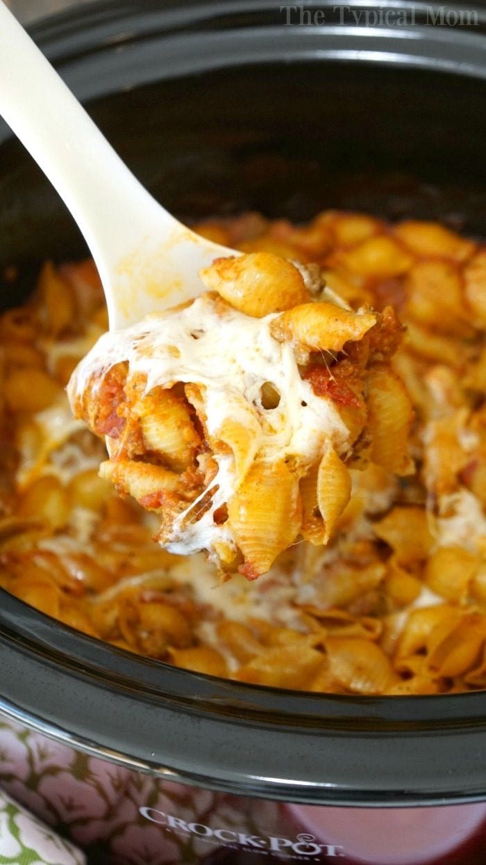A spoonful of cheesy pasta and sauce is being lifted from a crockpot lasagna, showcasing the good layers within.