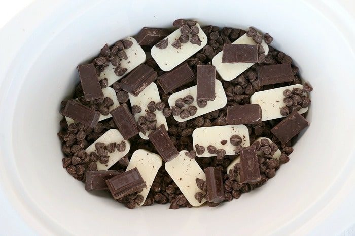 Chocolate chips, white candy melts, and chocolate pieces in a white bowl, ready to be melted for good crockpot peanut clusters.