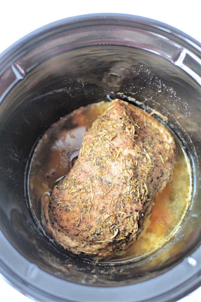A seasoned Porketta Roast is cooking slowly, melding flavors with its rich, savory juices.