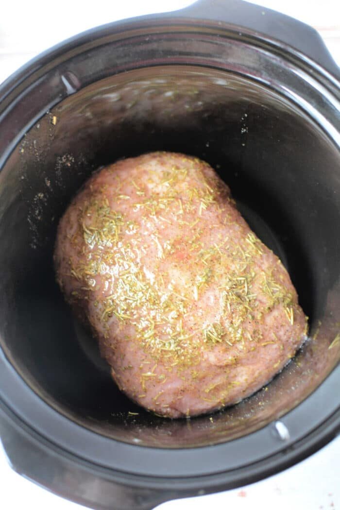A seasoned Porketta Roast rests in a sleek black slow cooker, ready for cooking.