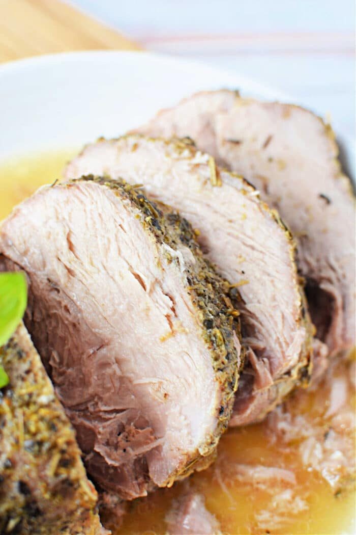 Sliced roasted porketta seasoned with herbs served on a white plate, garnished with a basil leaf.