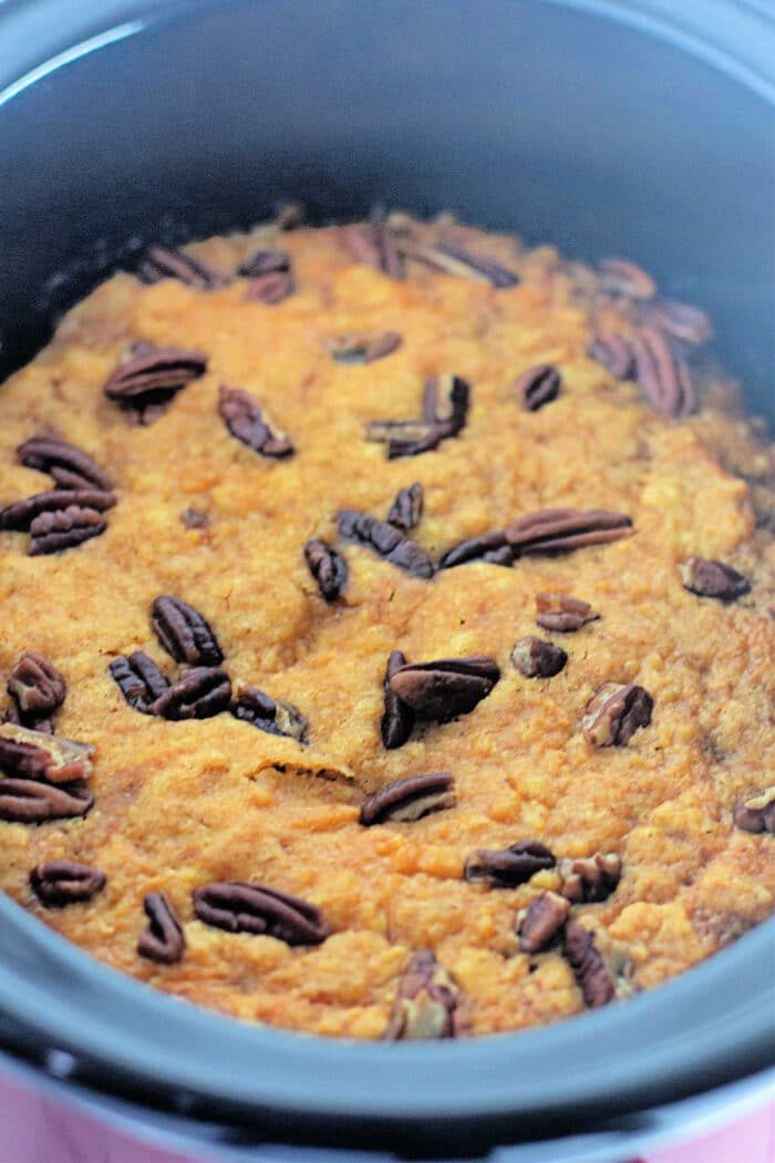 A close-up of pumpkin cake topped with pecans in a black crockpot, reminiscent of a comforting pumpkin dump cake.