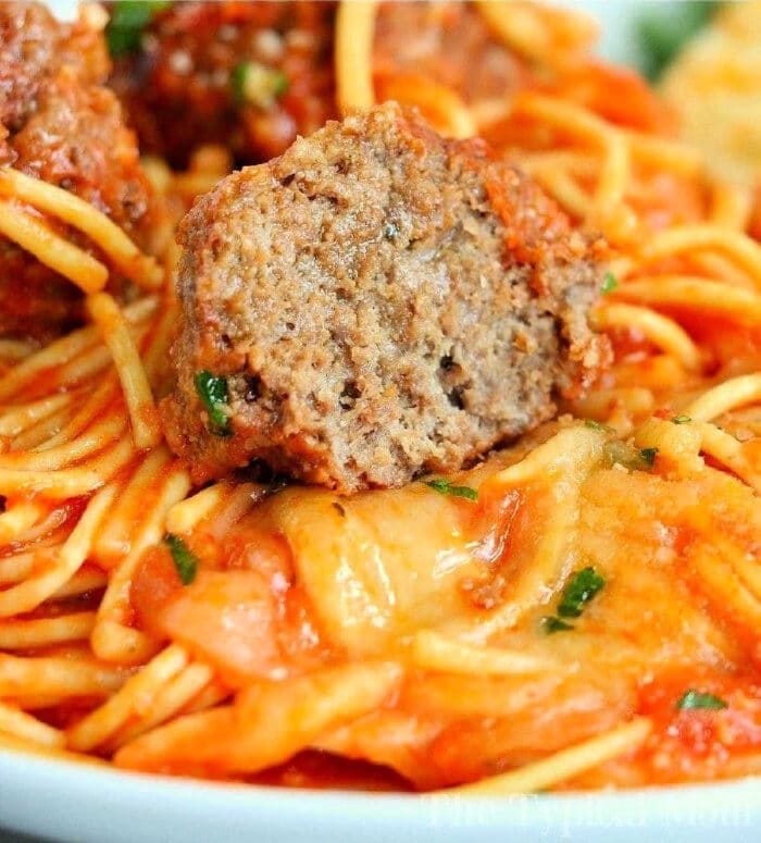 A close-up of crockpot spaghetti with jar sauce, topped with a sliced meatball and herbs.
