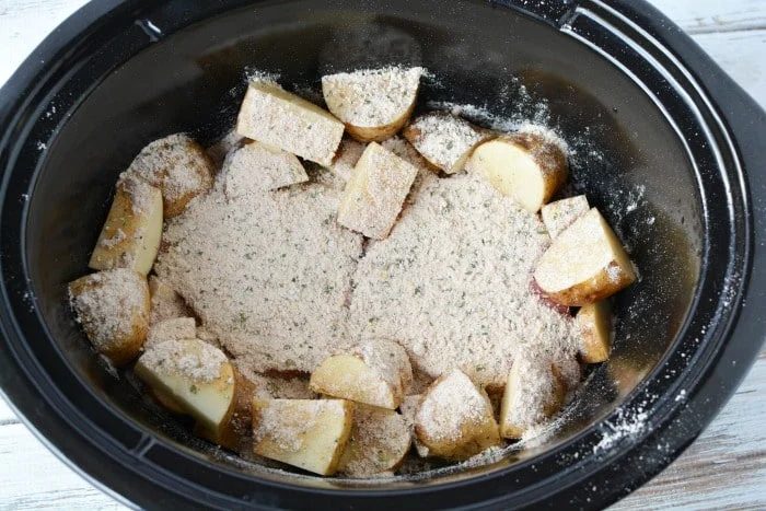 Sliced potatoes with seasoning nestle alongside tender crockpot steak in a black slow cooker.