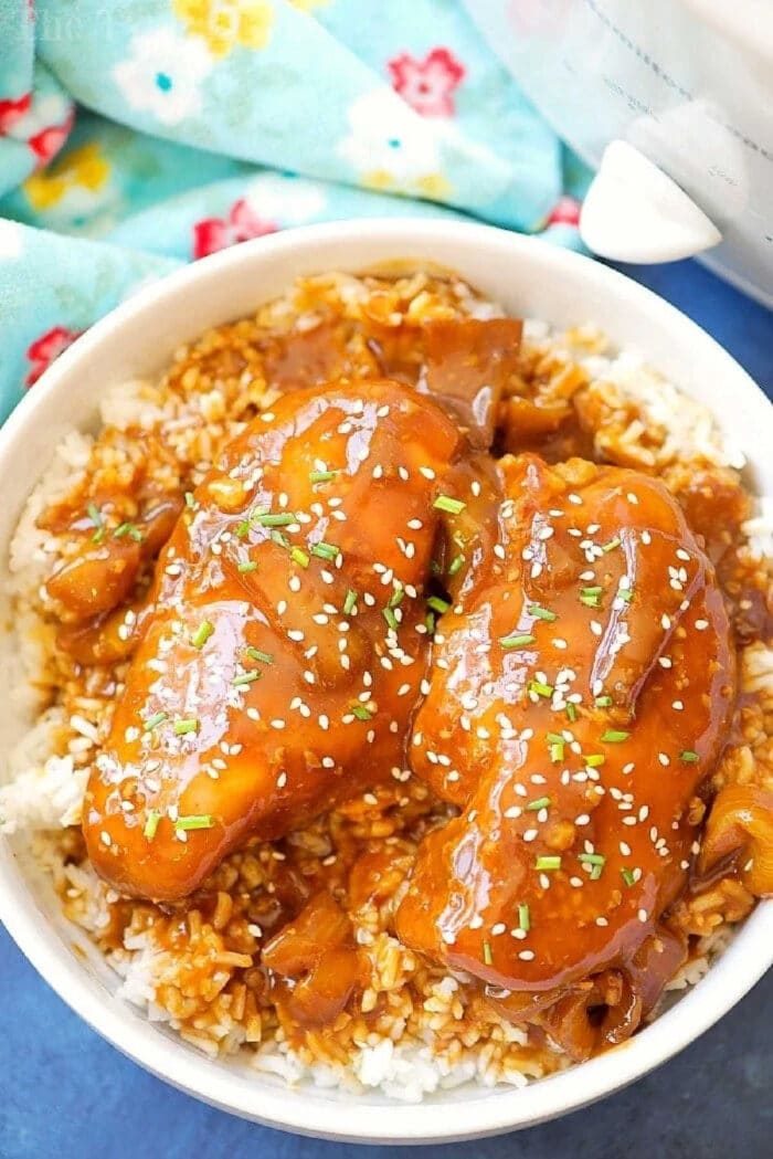Bowl of rice topped with crockpot teriyaki chicken, chopped herbs, sesame seeds, and a savory brown sauce.