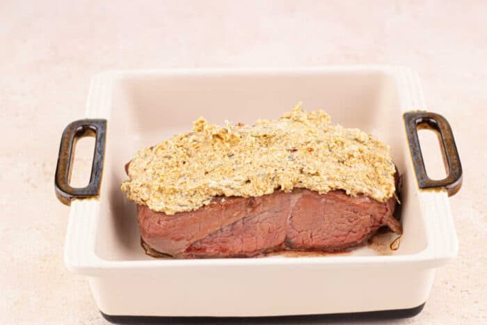 steak with a mustard and Parmesan crust in a white baking dish with handles.