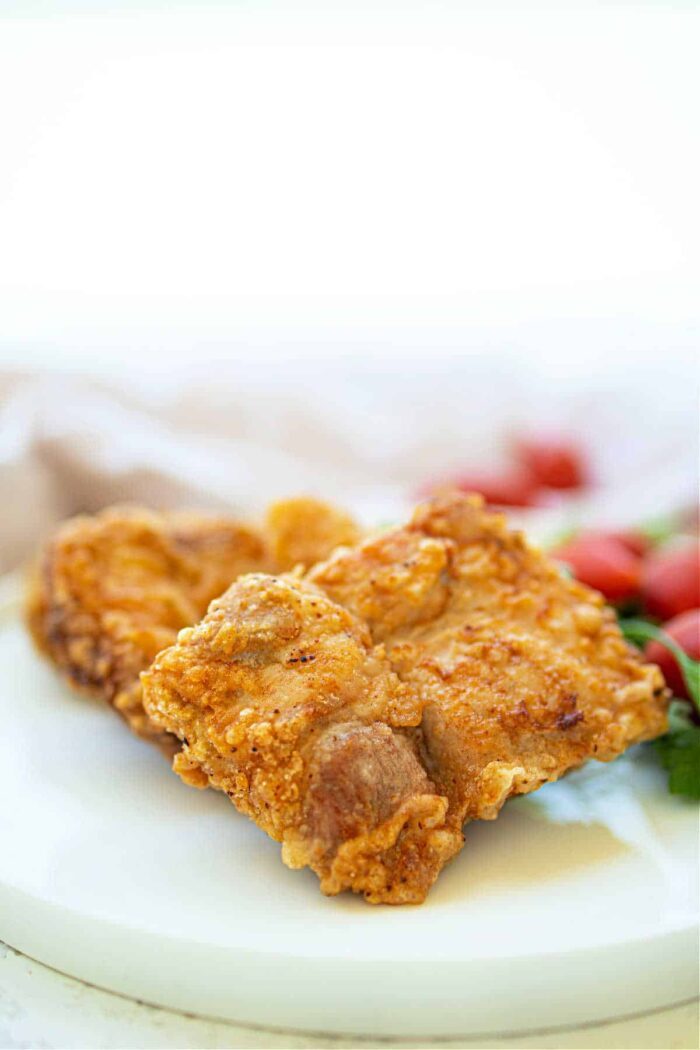 Crispy fried pork pieces share the plate with deep-fried pork chops, while cherry tomatoes brighten the background.