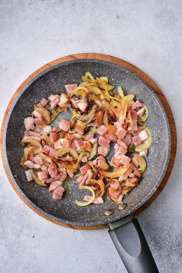 A frying pan with diced venison, sautéed onions, and tender slices of deer liver rests on a light gray background.