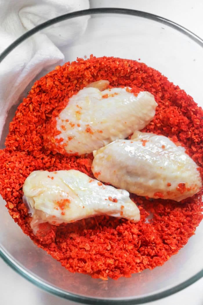Three uncooked chicken wings rest in a bowl of crushed doritos, echoing the zesty flavor of Doritos Ranch Dipped Hot Wings.