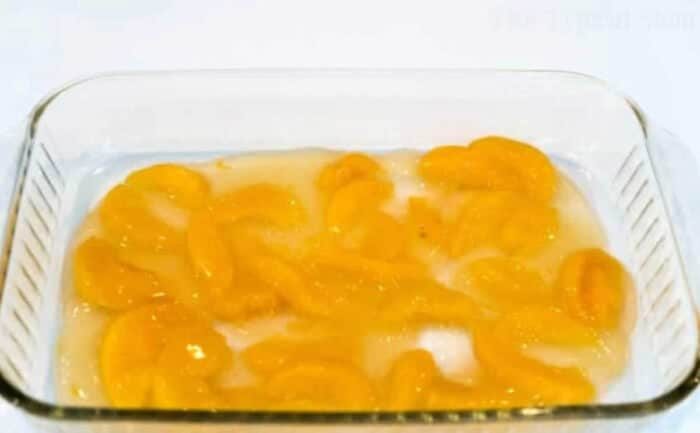 Glass dish with canned peach slices in syrup on a white surface, solid for making an effortless dump peach cobbler.