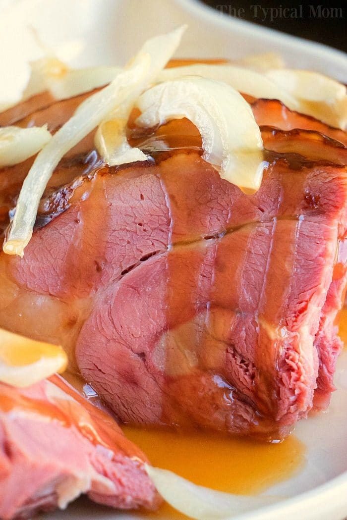 Close-up of glazed ham topped with sliced onions, reminiscent of a hearty Dutch oven ham.