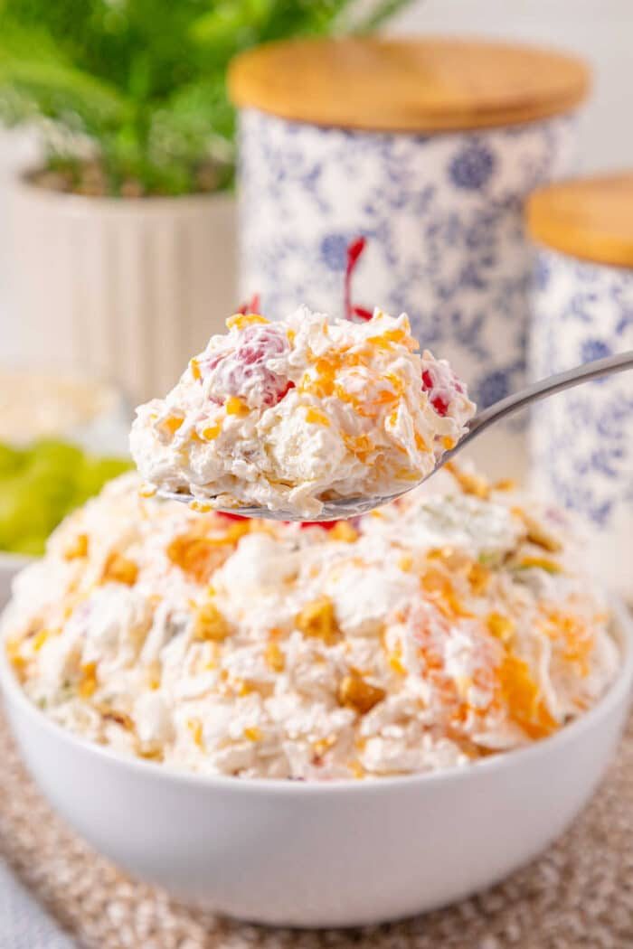 A spoonful of creamy fruit salad held above a bowl filled with the same salad, showcasing this easy ambrosia recipe.