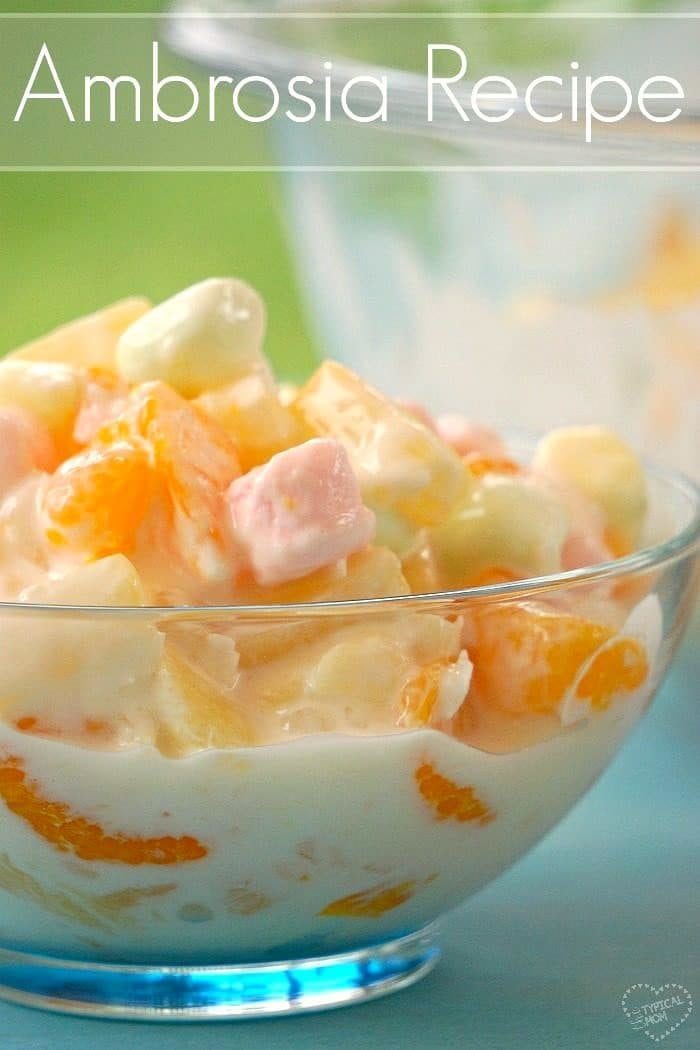 Bowl of creamy, easy ambrosia salad with fruit and pastel marshmallows. Text at the top reads Easy Ambrosia Recipe.