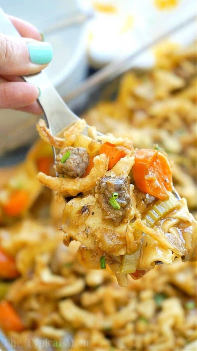A fork holding a bite of easy beef stew casserole with noodles, beef, carrots, celery, and crispy onions.