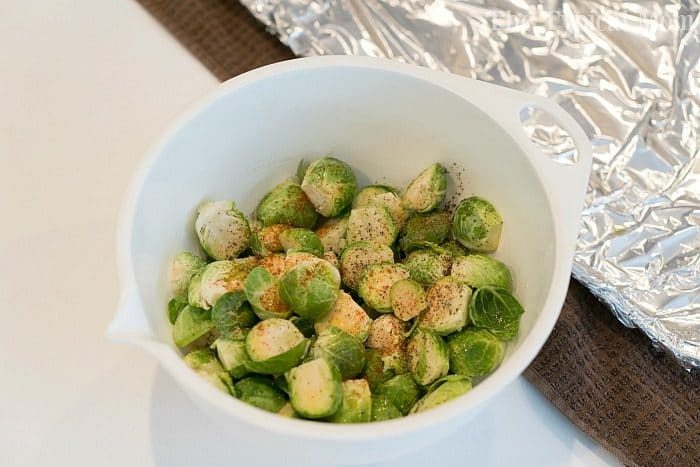 A bowl of seasoned halved Brussels sprouts sits on the kitchen counter, ready to be baked. Wondering how long to bake Brussels sprouts at 450 degrees? They'll become perfectly crispy in about 20-25 minutes.