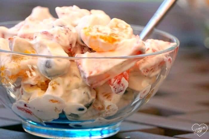 A glass bowl of creamy fruit salad with Cool Whip and a spoon.