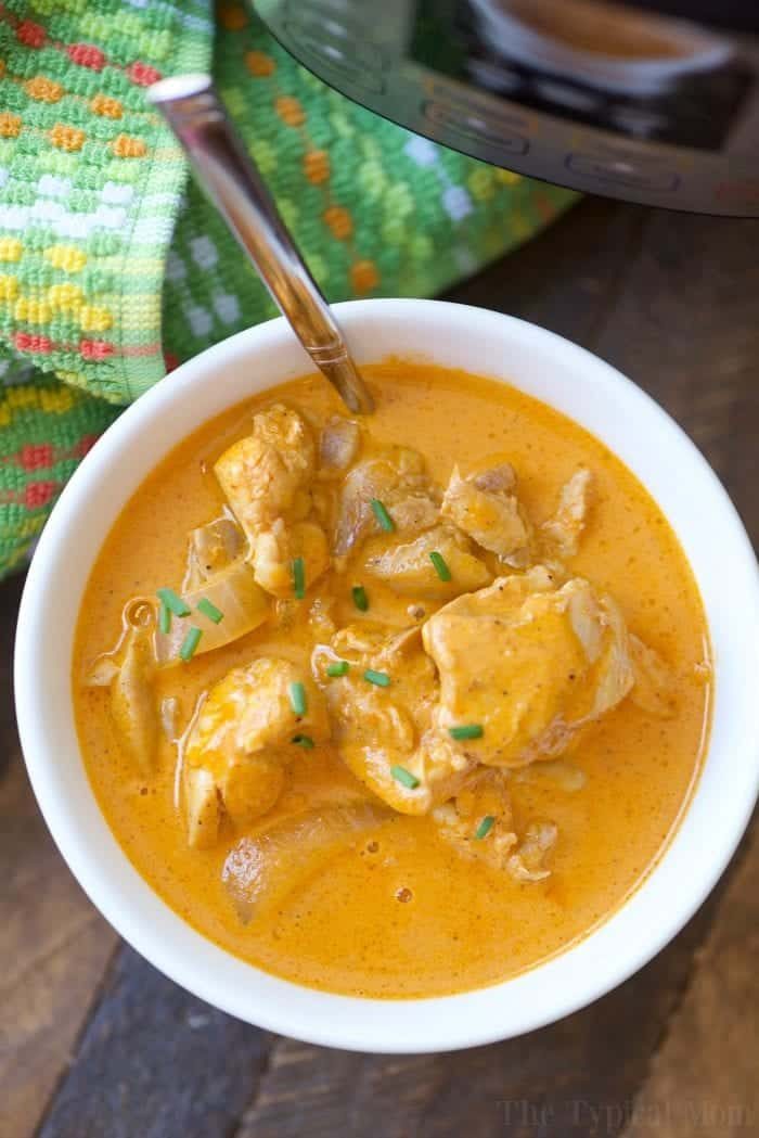 A bowl of creamy chicken curry, one of those easy instant pot chicken recipes, garnished with herbs. A spoon and a colorful cloth sit nearby, ready for a delightful meal experience.