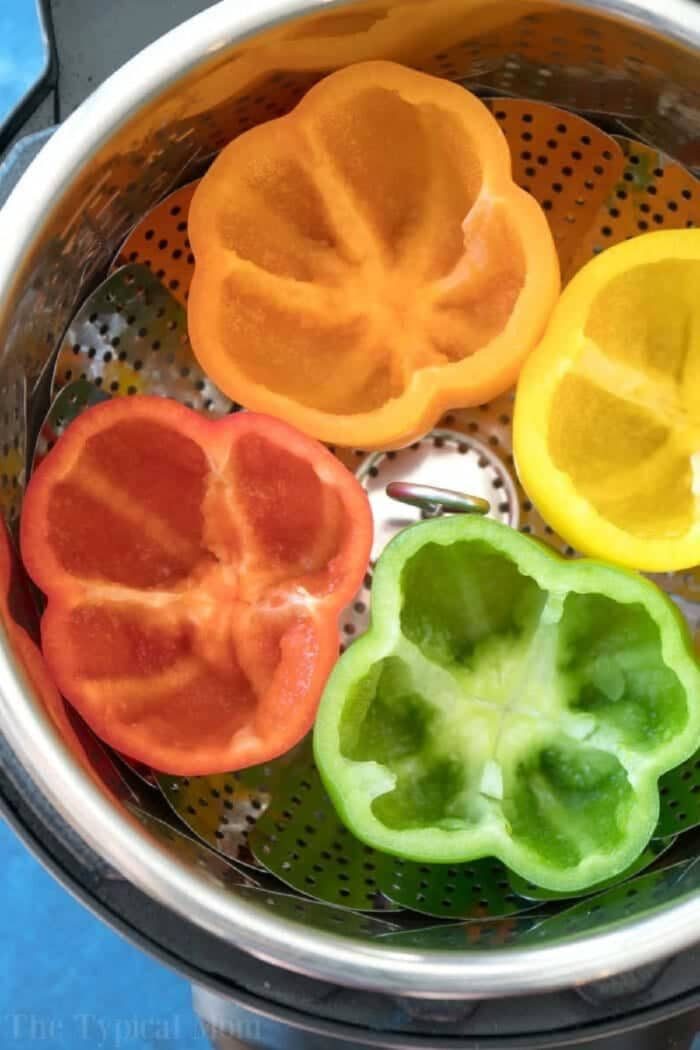 Four hollowed bell pepper halves—orange, yellow, red, and green—in a steamer basket, ready for easy Instant Pot stuffed peppers.