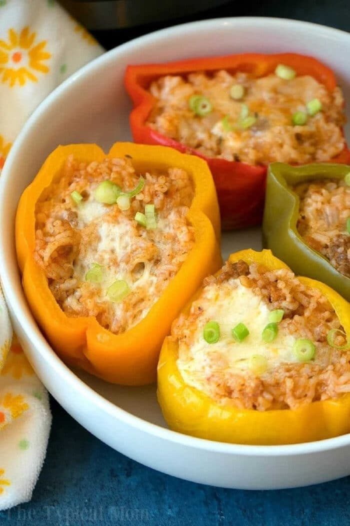 Three colorful easy Instant Pot stuffed peppers filled with rice, cheese, and green onions, served in a white bowl.