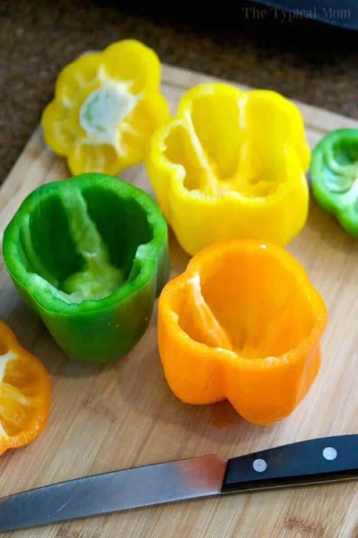 Hollowed green, yellow, and orange bell peppers on a cutting board with a knife, ready for easy Instant Pot stuffed peppers.