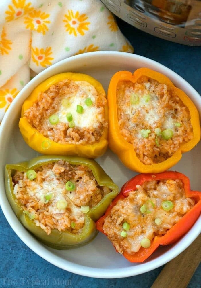 Four easy Instant Pot stuffed peppers, filled with rice, cheese, and scallions, are served in a white bowl for a quick and good meal.