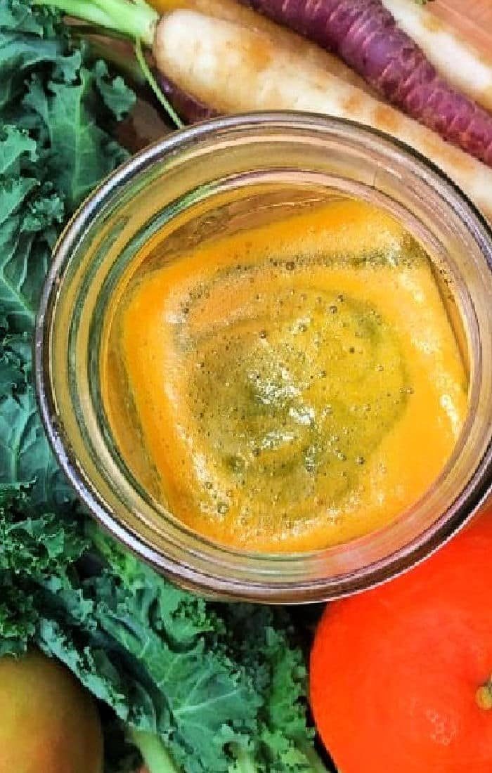 Easy kale juice with orange smoothie, surrounded by fresh kale, crisp carrots, and a juicy apple.