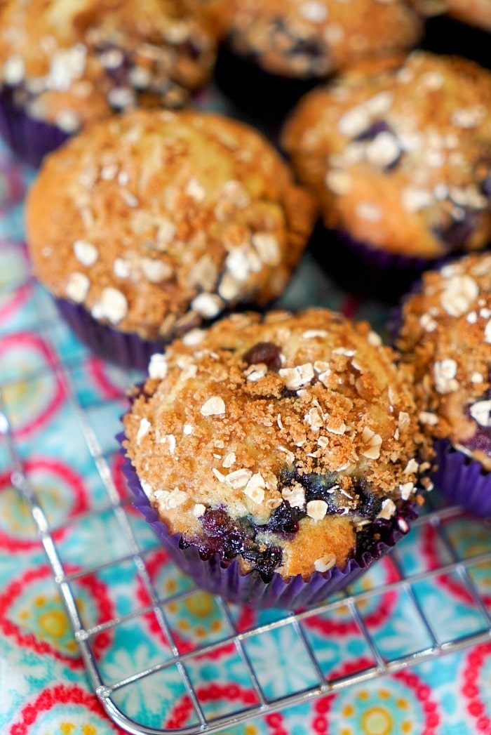 Blueberry muffins with oat crumble topping on a wire cooling rack, colorful patterned cloth underneath—an easy muffin recipe solid for any occasion.