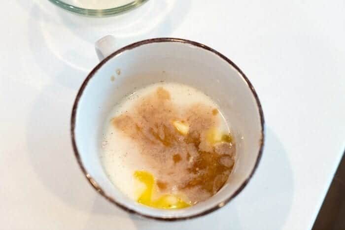 A white mug with milk, melted butter, cinnamon, and sugar on a white surface—solid ingredients for an easy mug cake recipe.